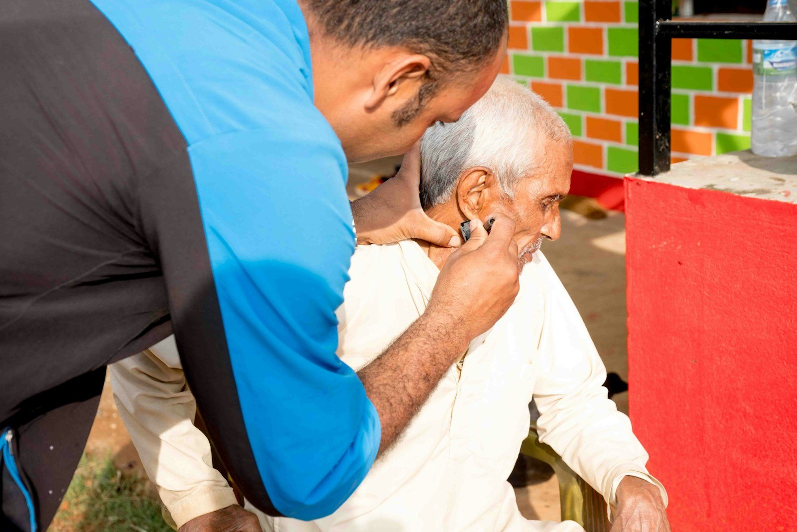 a man getting his hair cut by a man in a blue shirt